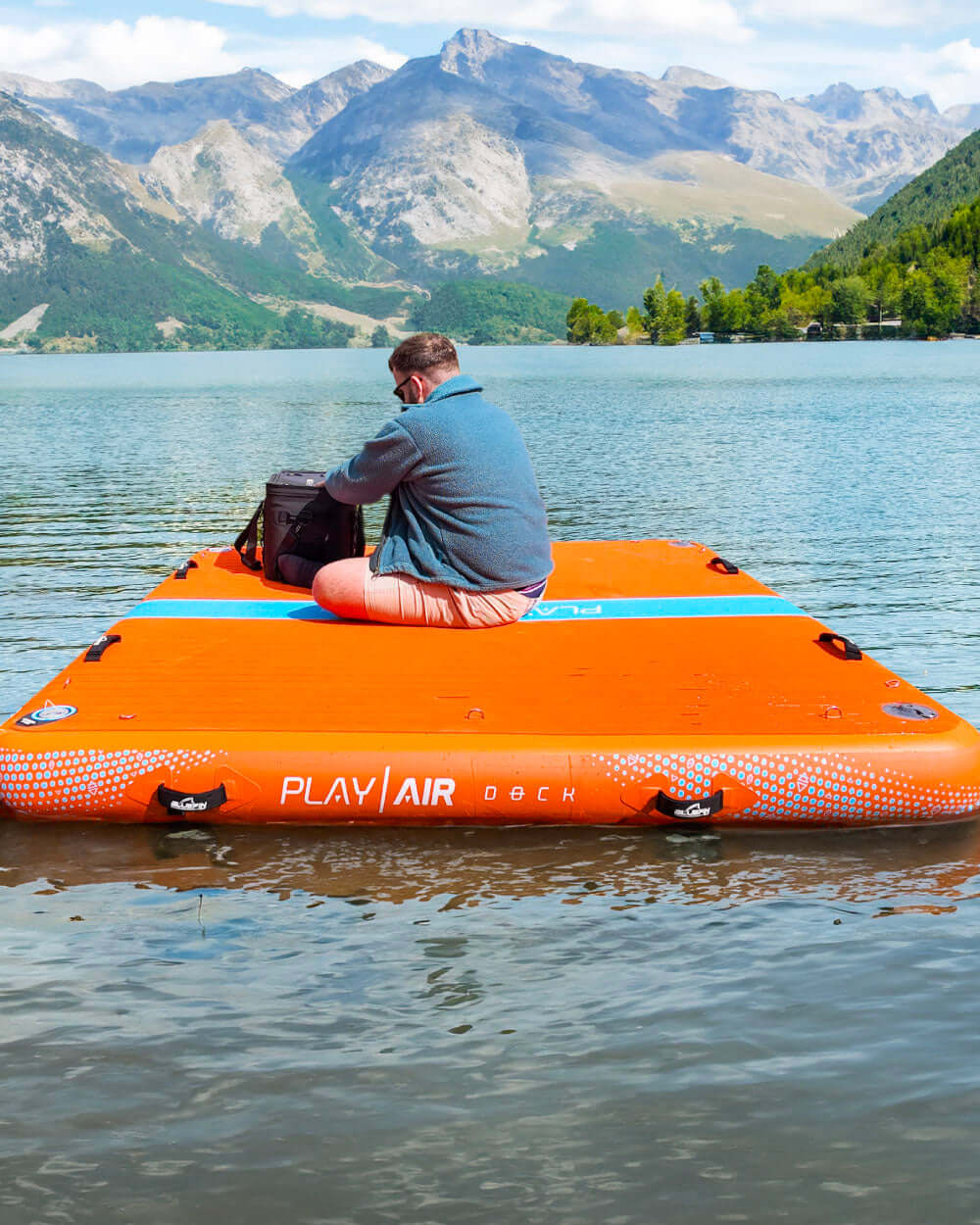 Person sitting on an inflatable play air dock in a lake with mountains in the background