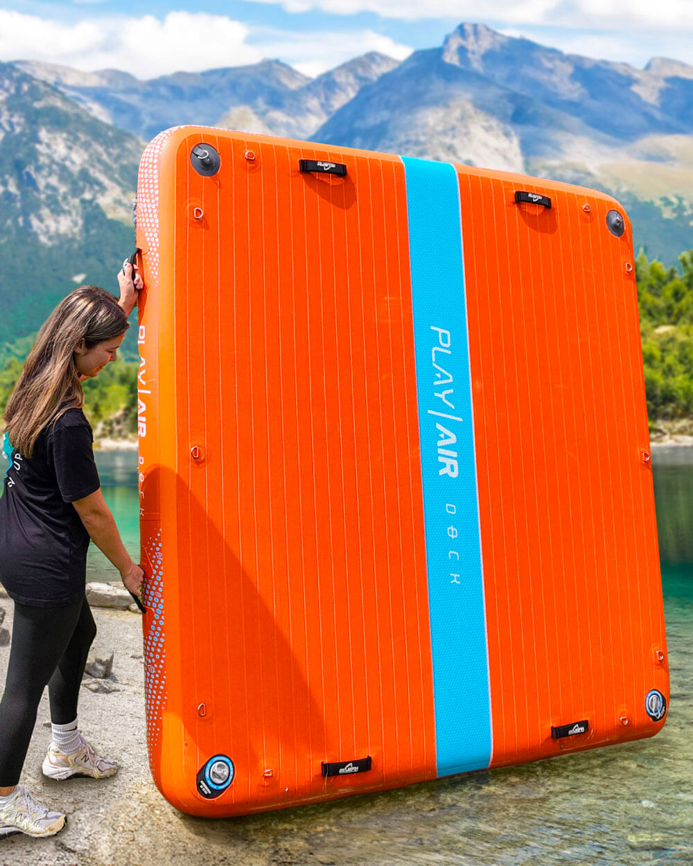Orange inflatable play air dock with blue stripe held by a person against a mountainous background