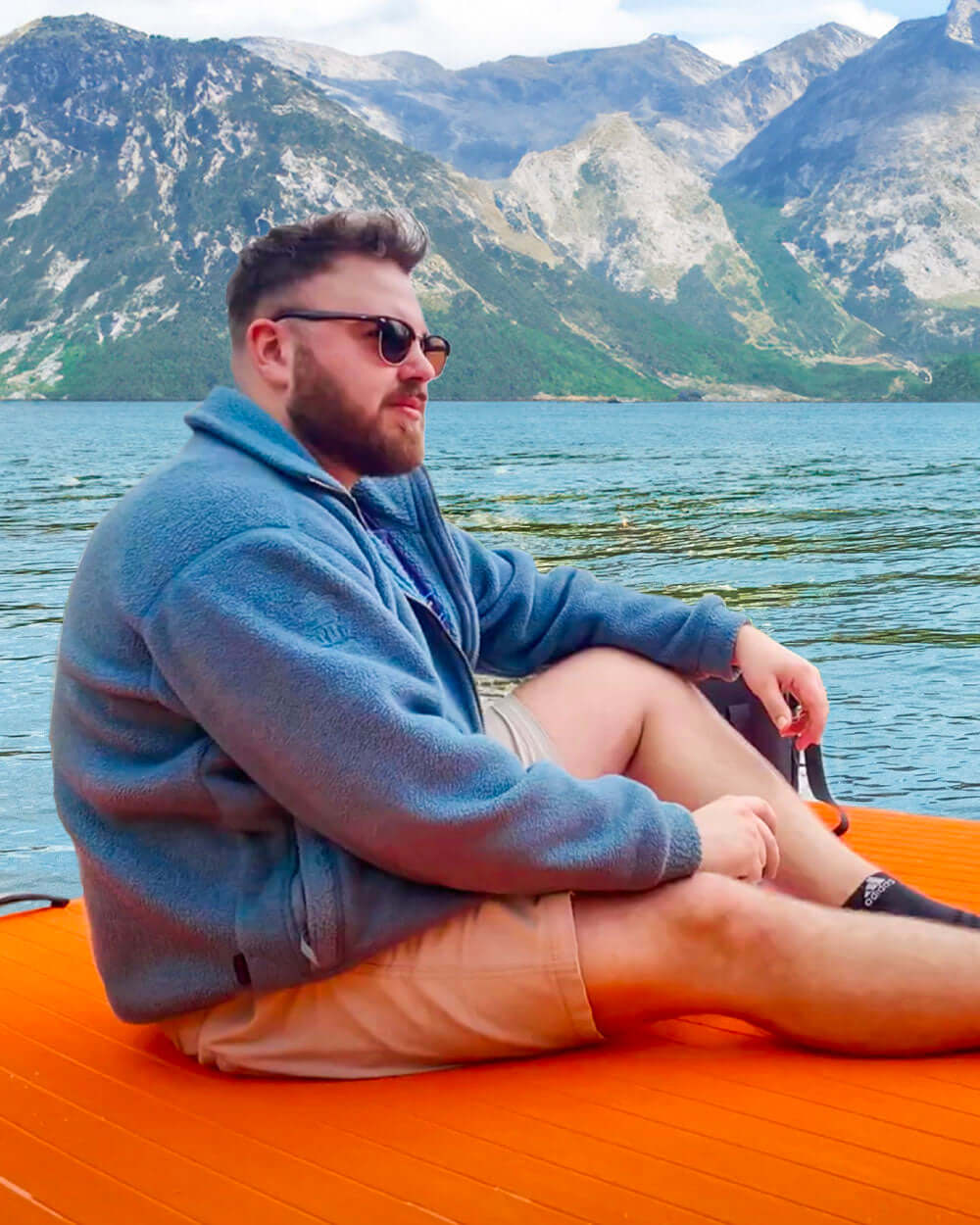 Man sitting on an orange play air dock by a lake with mountains in the background