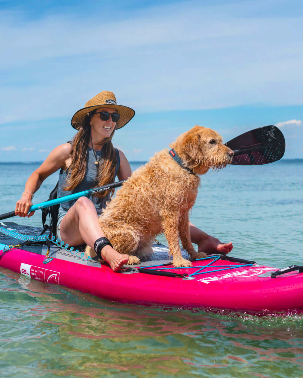 Woman and dog on a pink stand-up paddleboard in the ocean with a clear blue sky using the attachable kayak seat