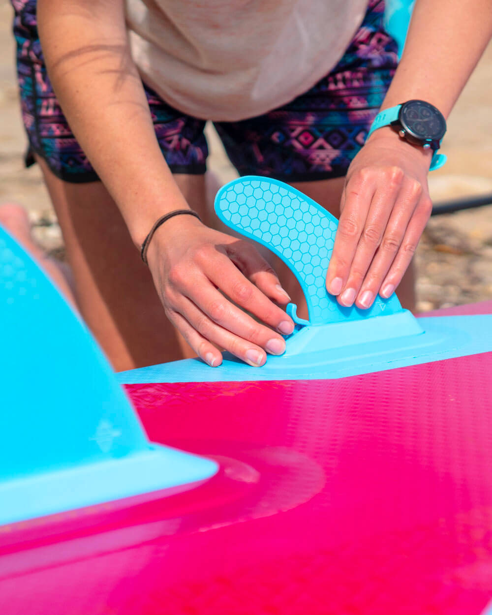 Person applying a blue smartlock fin to a bluefin berry red cruise paddle board
