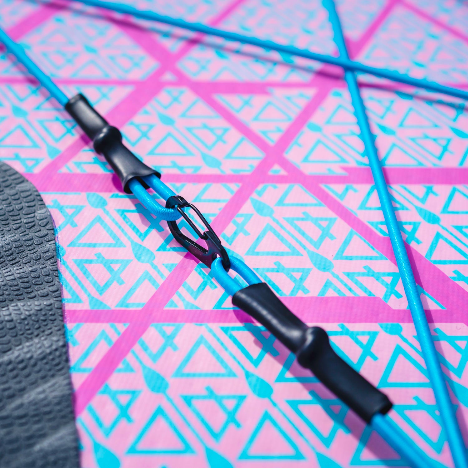 Close-up of a colorful paddleboard deck with blue straps and a black connector on a patterned surface.