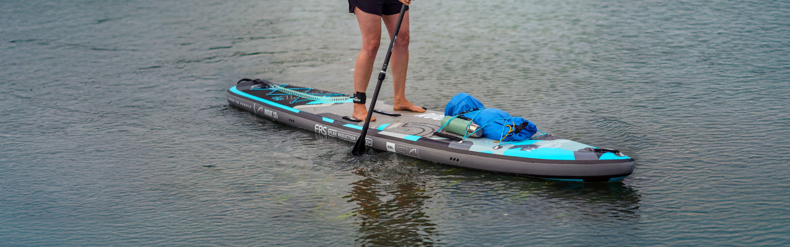 Person paddleboarding on a Bluefin SUP, with gear secured, gliding over calm water.