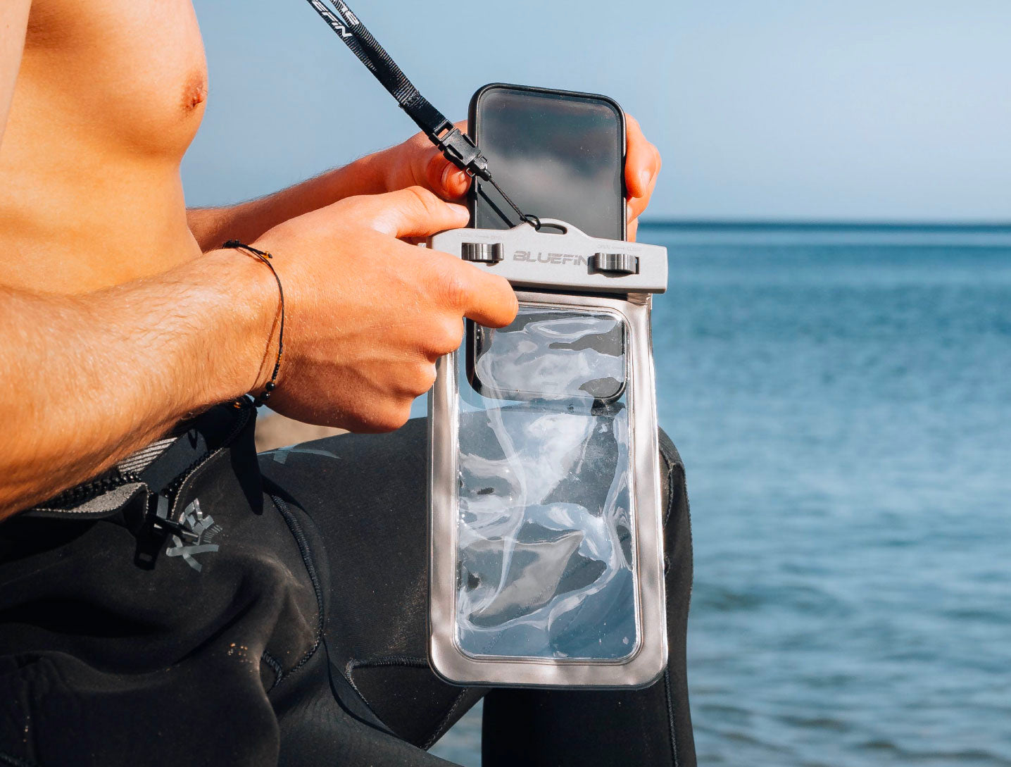 Man holding a waterproof phone case by the water, ideal for outdoor adventures.