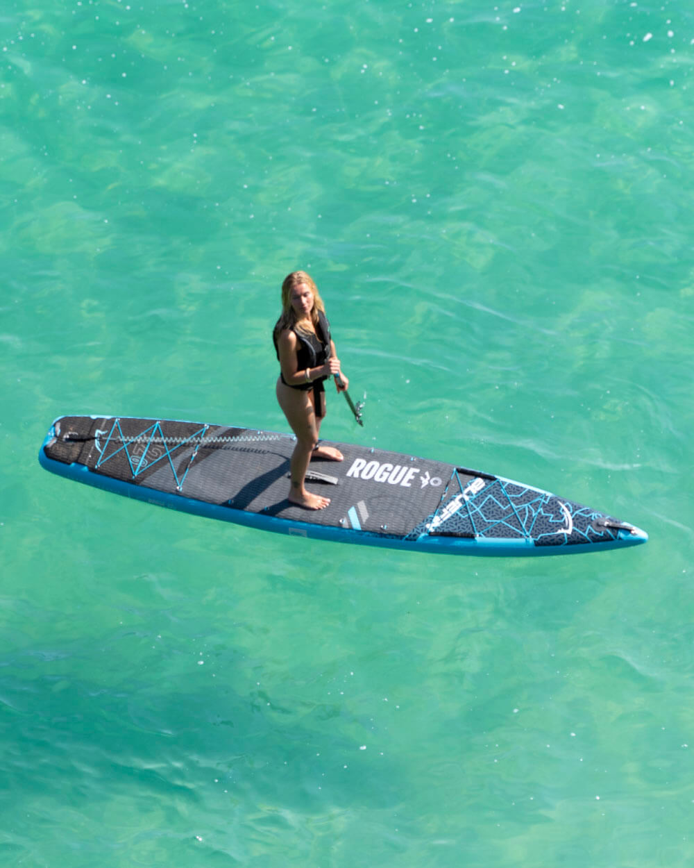 Paddleboarder on a turquoise sea, holding a paddle on a Rogue SUP. Ideal for water sports enthusiasts.