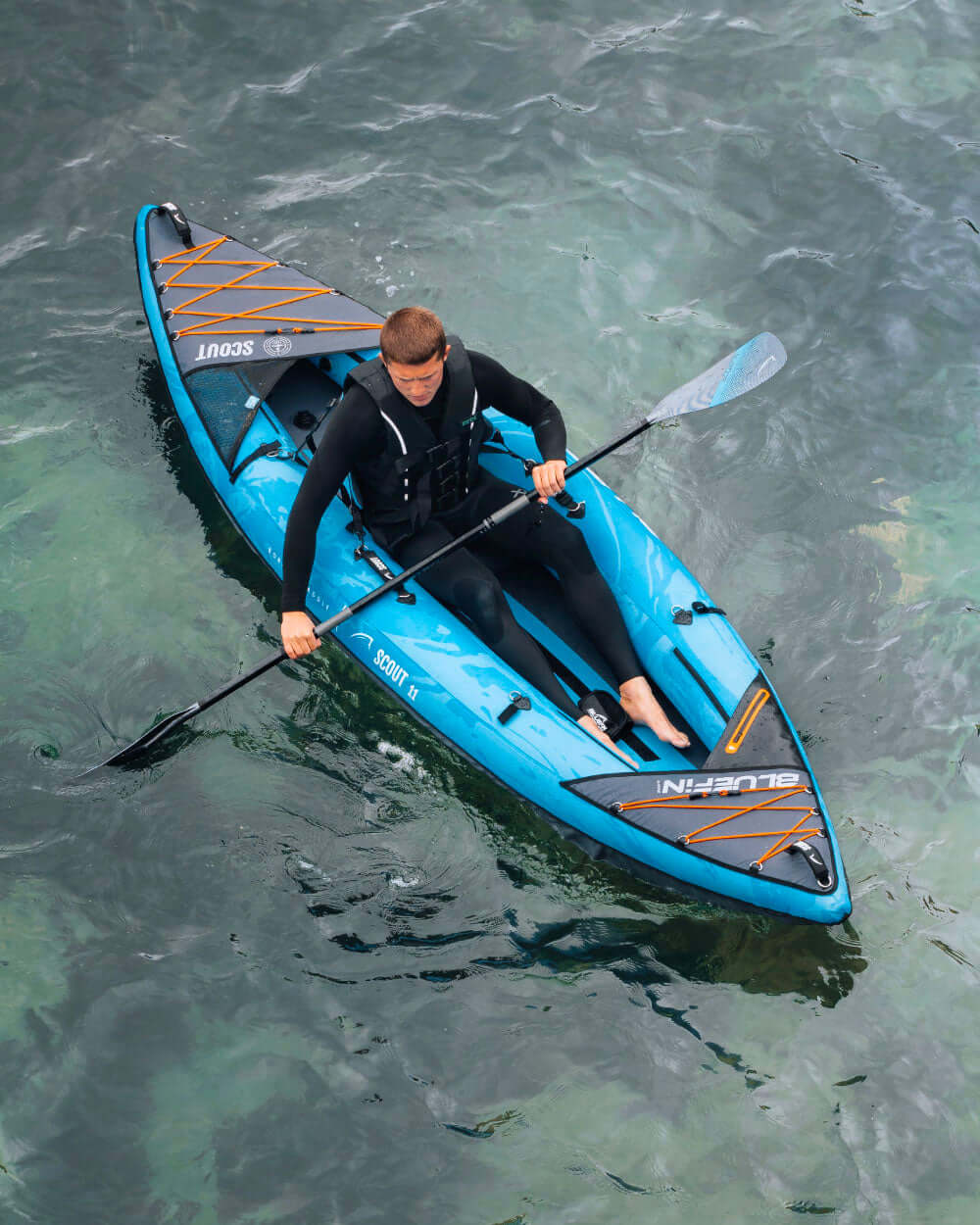 Person kayaking on a blue inflatable SUP in clear water, wearing a wetsuit and paddling.