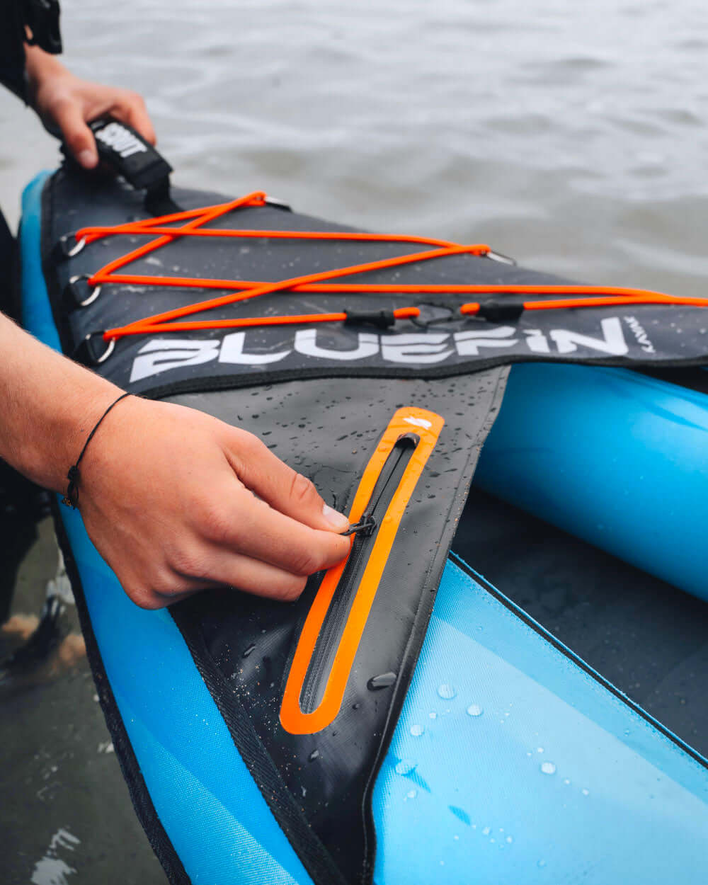 Person adjusting the zipper on a Bluefin SUP kayak by the water's edge.