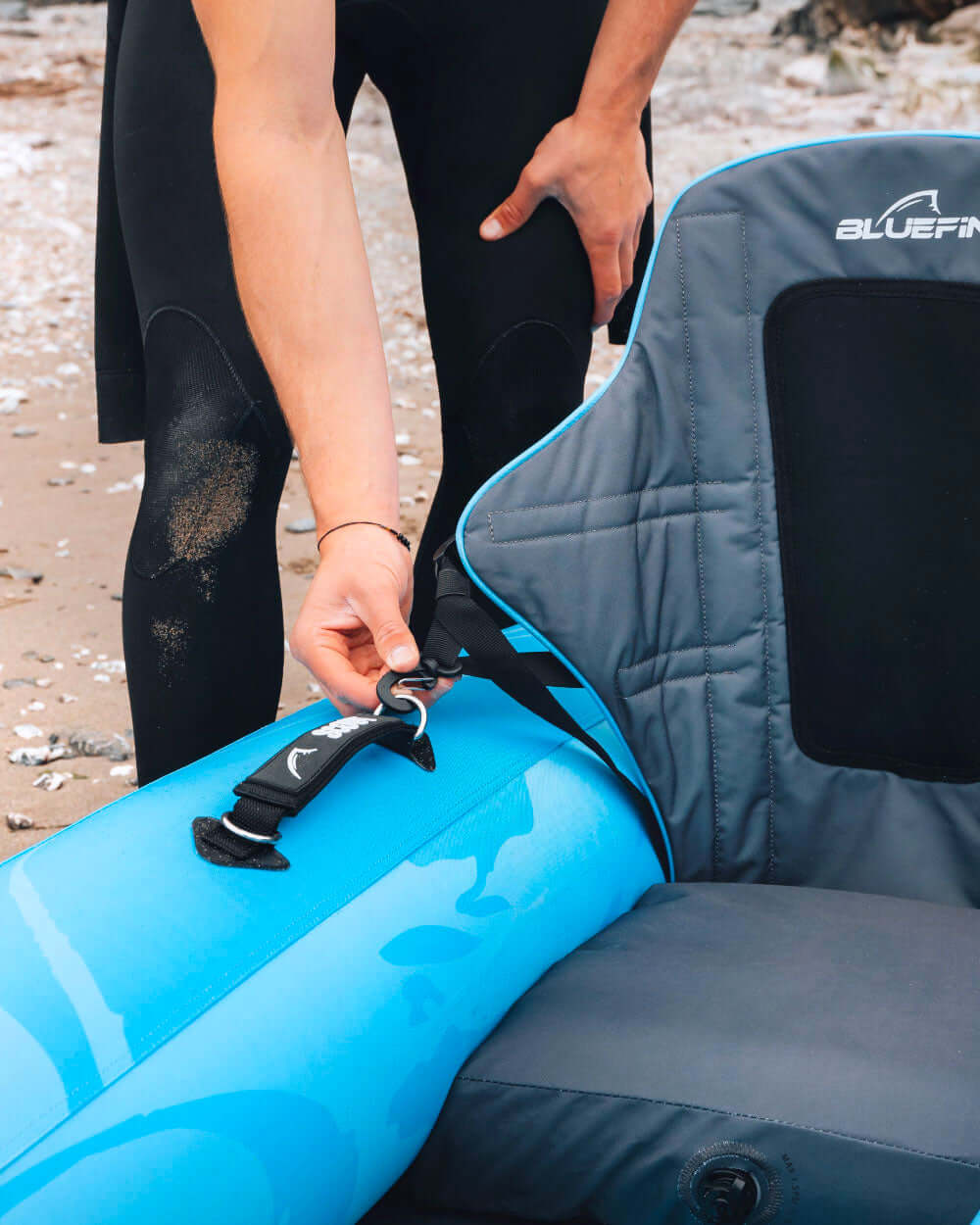 Person adjusting the strap on a Bluefin SUP seat by the beach.