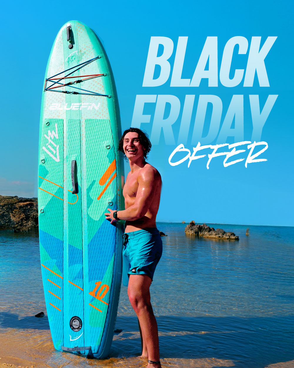 Person smiling while holding a blue-green inflatable paddleboard on a beach with clear water