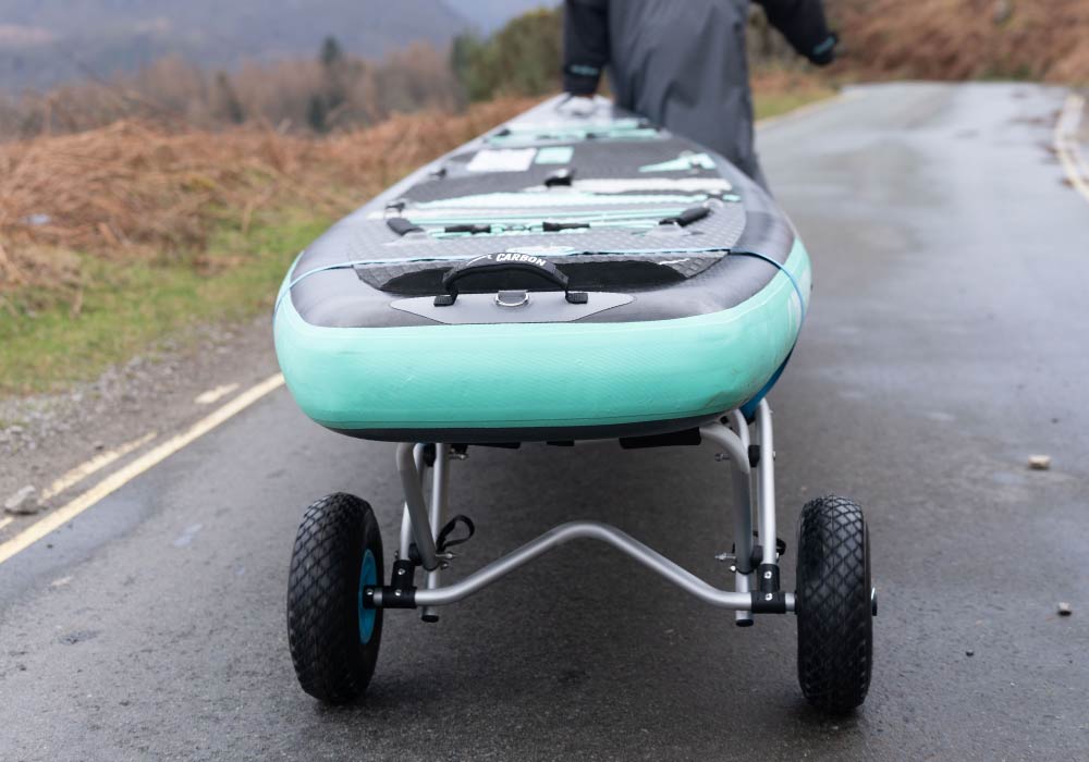 Inflatable stand-up paddleboard with durable wheels, parked on a wet road. Ideal for water adventure.