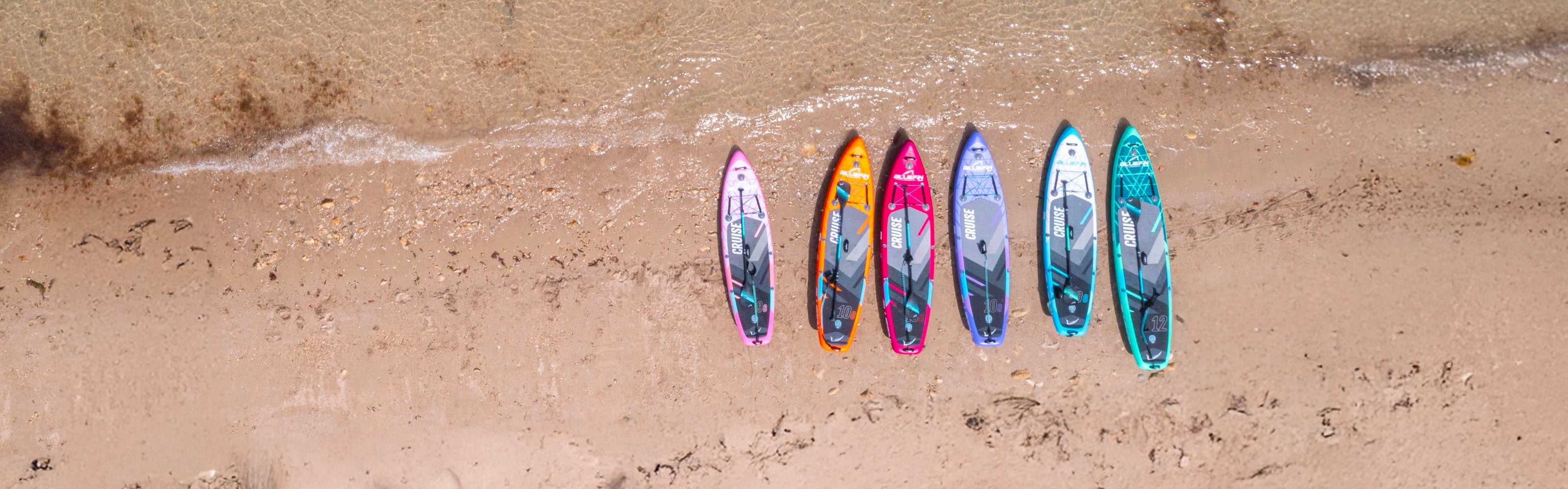 Colorful stand-up paddleboards lined up on a sandy beach near calm water.
