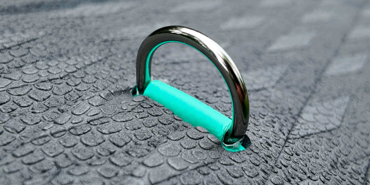 Close-up of a turquoise paddleboard D-ring embedded in textured gray material.
