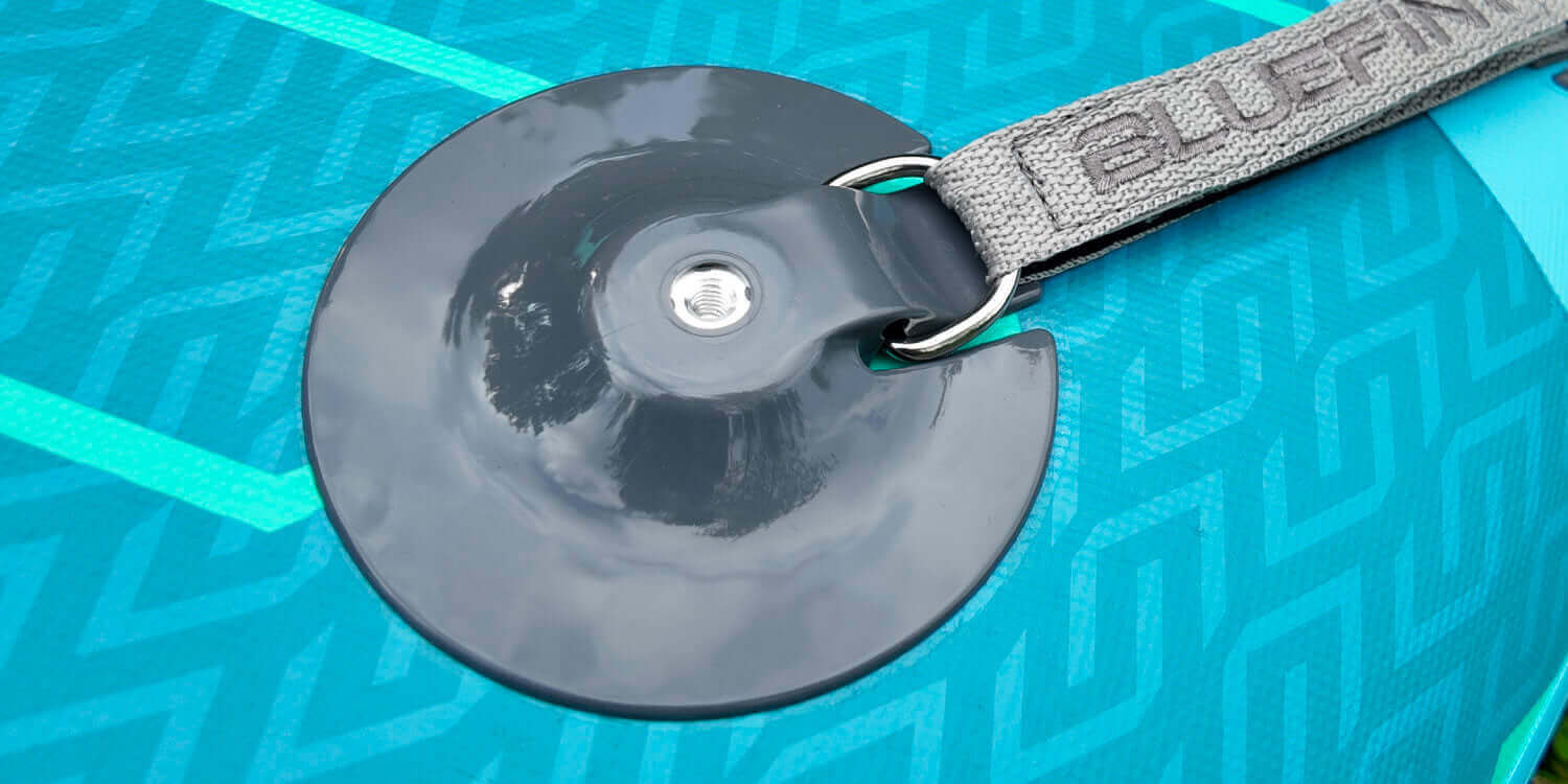 Close-up of a Bluefin SUP paddleboard's fin attachment on a textured turquoise surface.