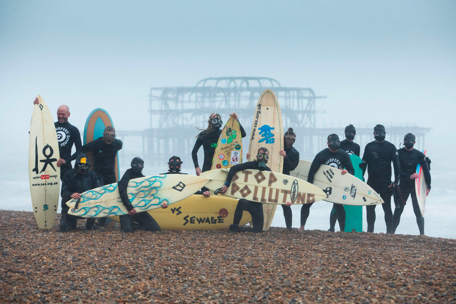 Activists in wetsuits with surfboards, promoting ocean conservation, on a foggy beach.