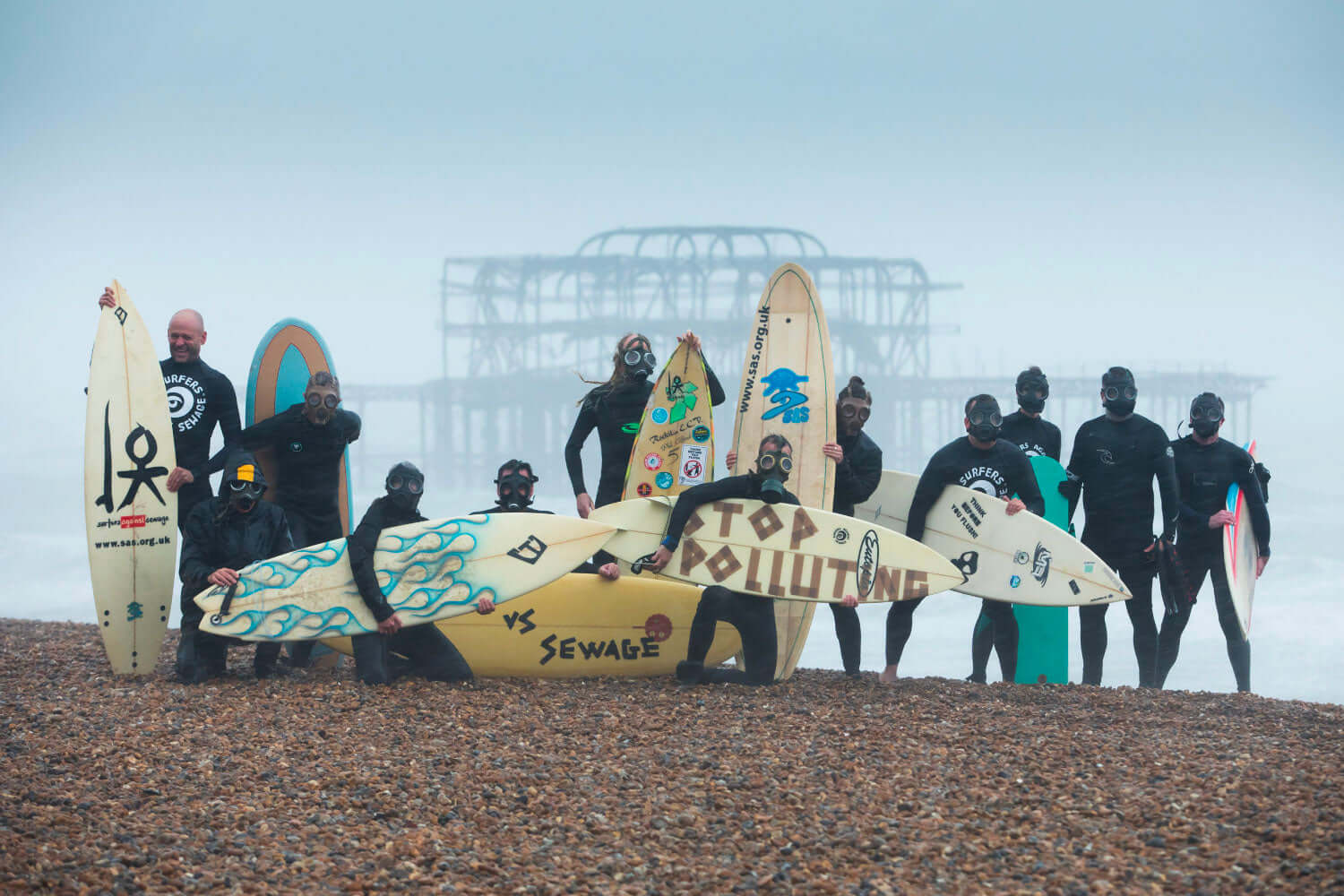 Activists in wetsuits with surfboards, promoting ocean conservation, on a foggy beach.