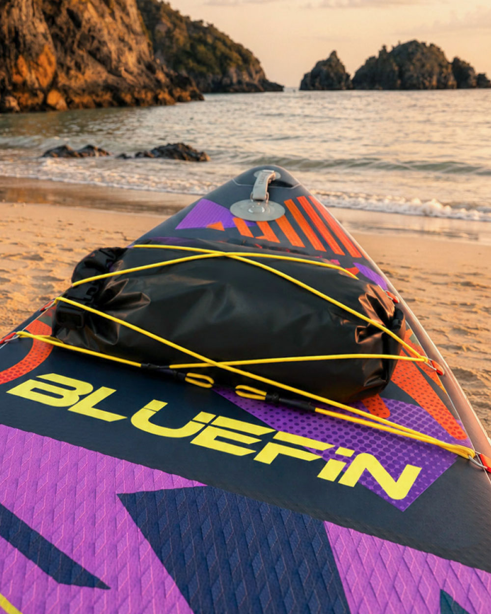 Inflatable paddleboard on sandy beach with black dry bag and colorful graphics at sunset