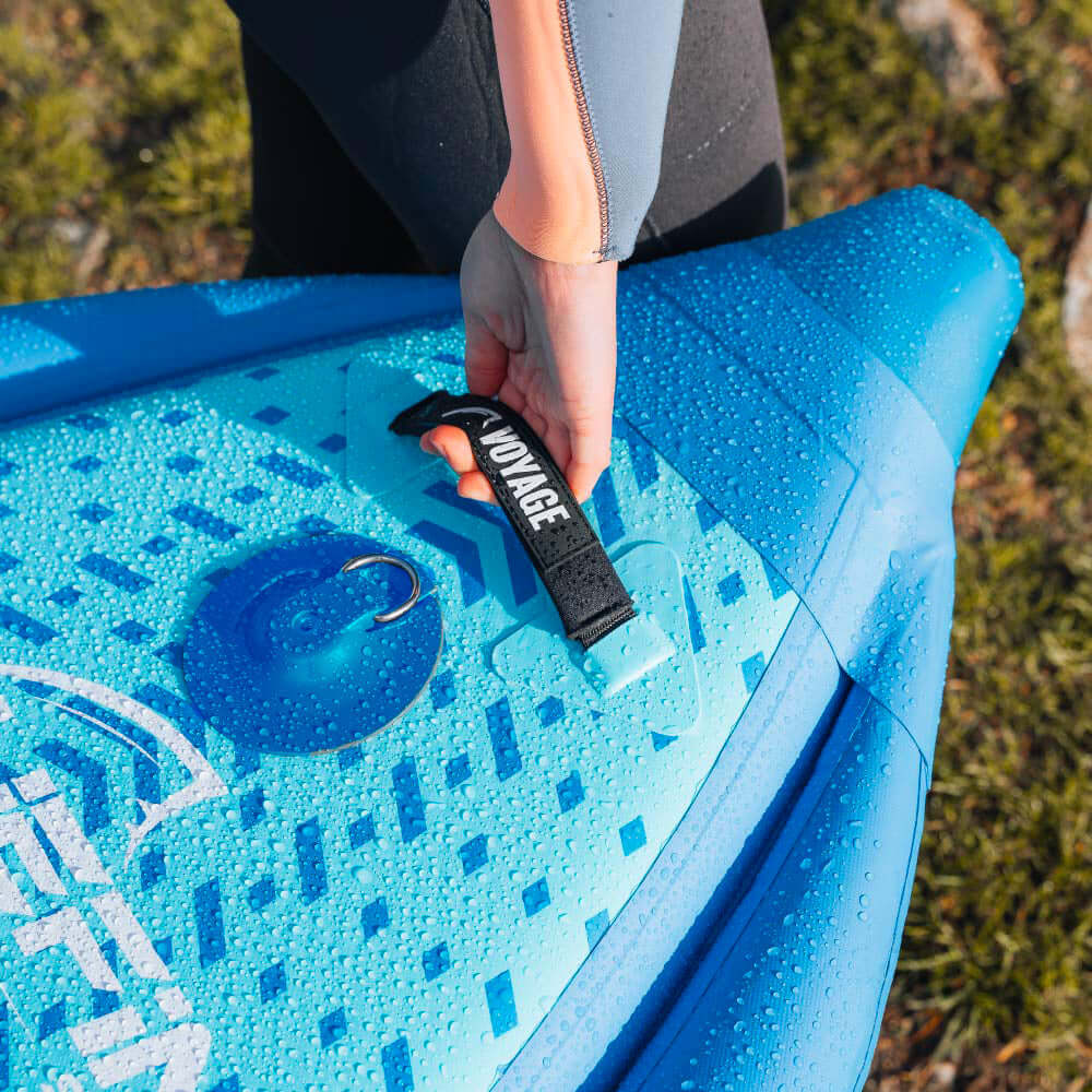 Hand holding a black strap on a blue stand-up paddleboard with water droplets.