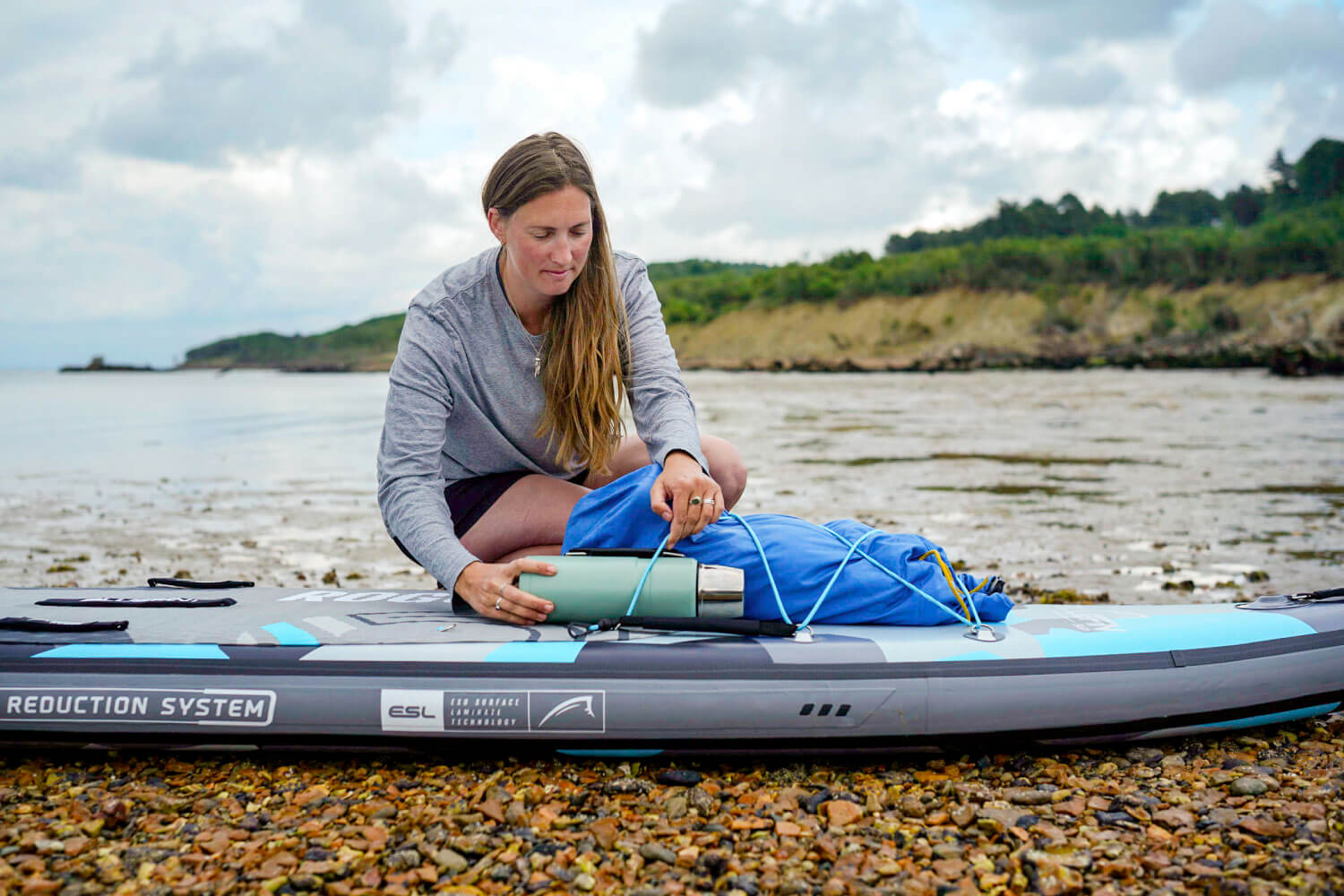 Woman packing gear on an inflatable stand-up paddleboard by the shore, preparing for an adventure.