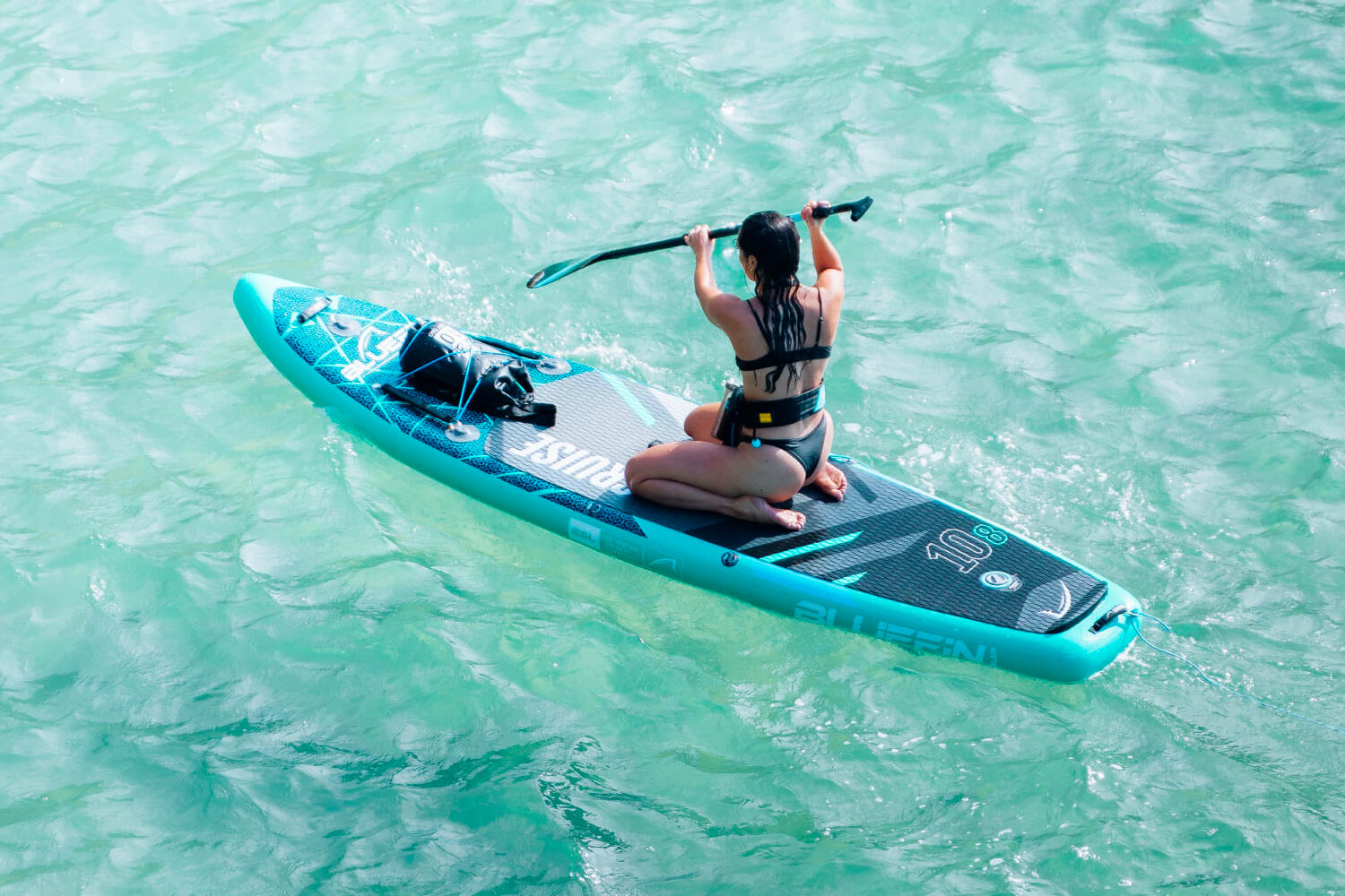 Woman paddling on a Bluefin stand-up paddleboard in clear water.