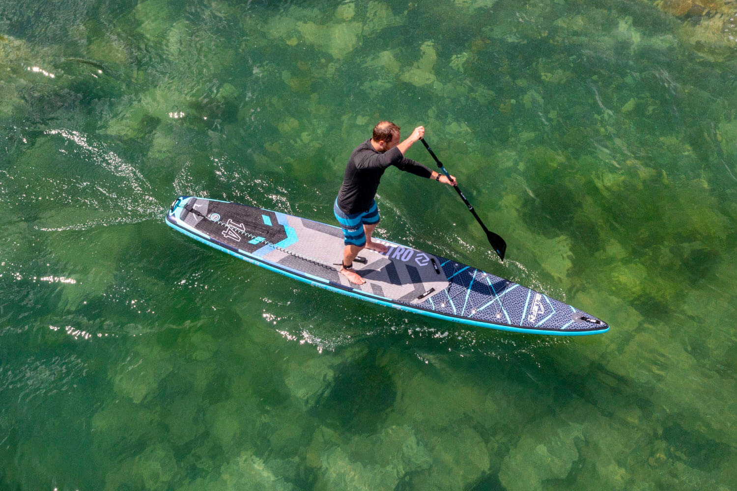 Man paddleboarding on clear water with a blue and gray paddleboard.