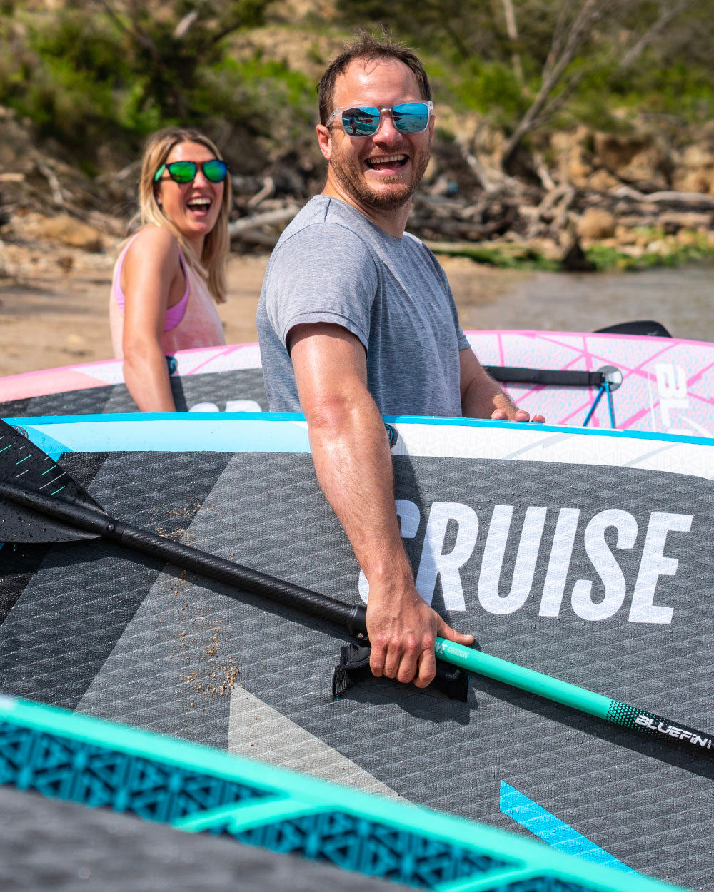 Two people with bluefin stand-up paddleboards on a beach