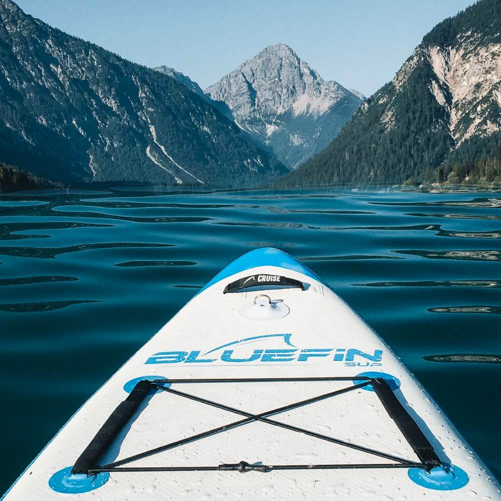 Bluefin SUP paddle board on tranquil water, surrounded by stunning mountain scenery. Ideal for outdoor adventures.