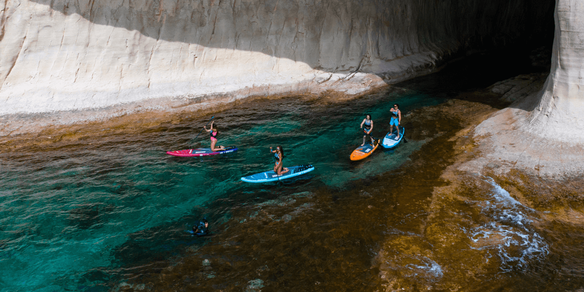 four people paddleboarding next to cliffs