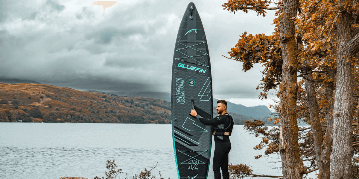 man holding onto a paddleboard, overlooking a lake 