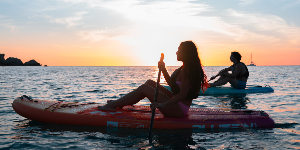 Two people paddleboarding into sunset 