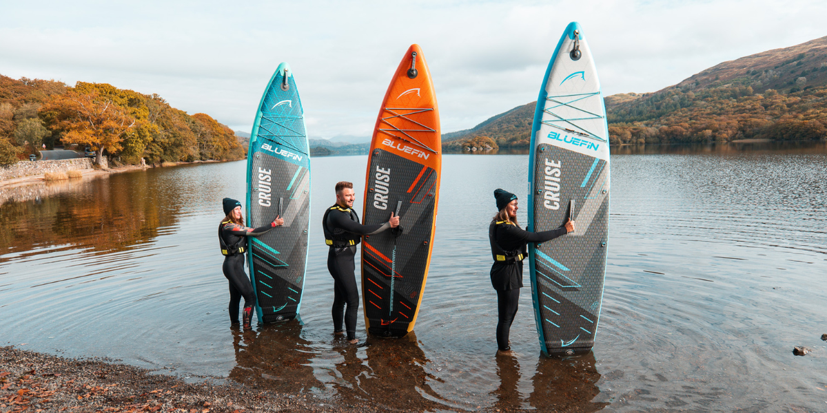 three people holding paddleboards at the front of a lake