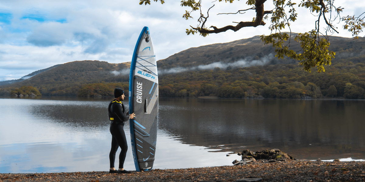man holding a paddleboard infant of an autumnal lake