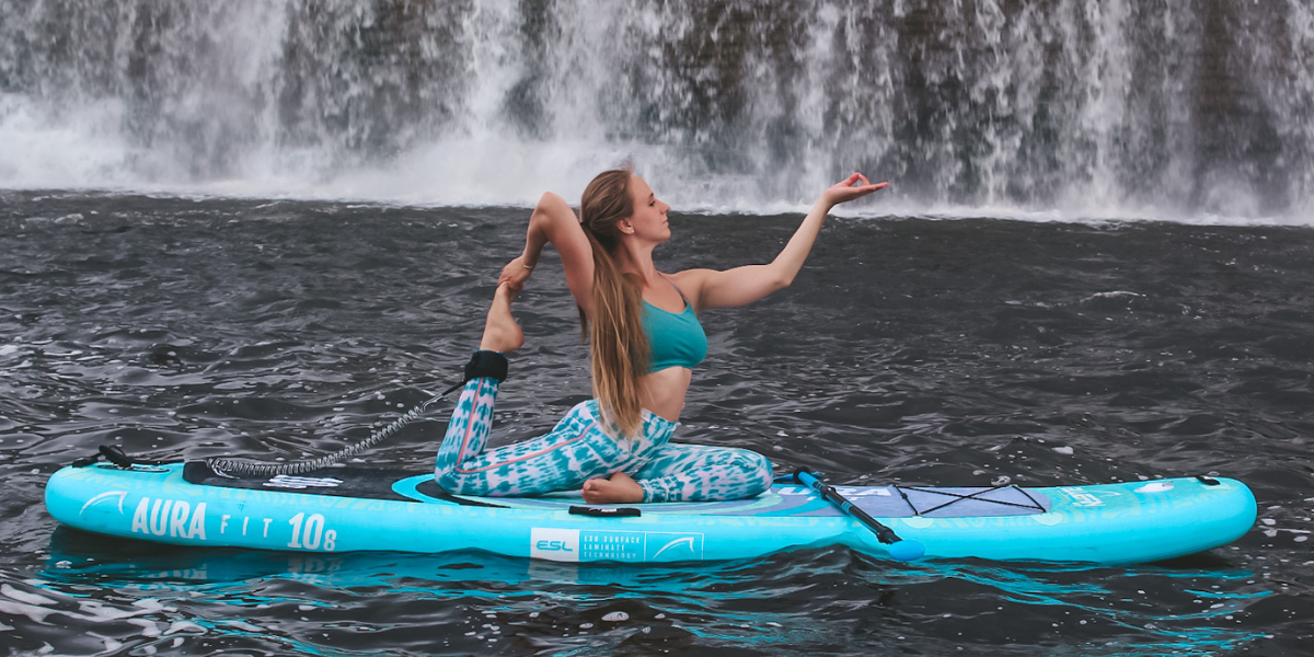 A woman doing sup yoga near a waterfall