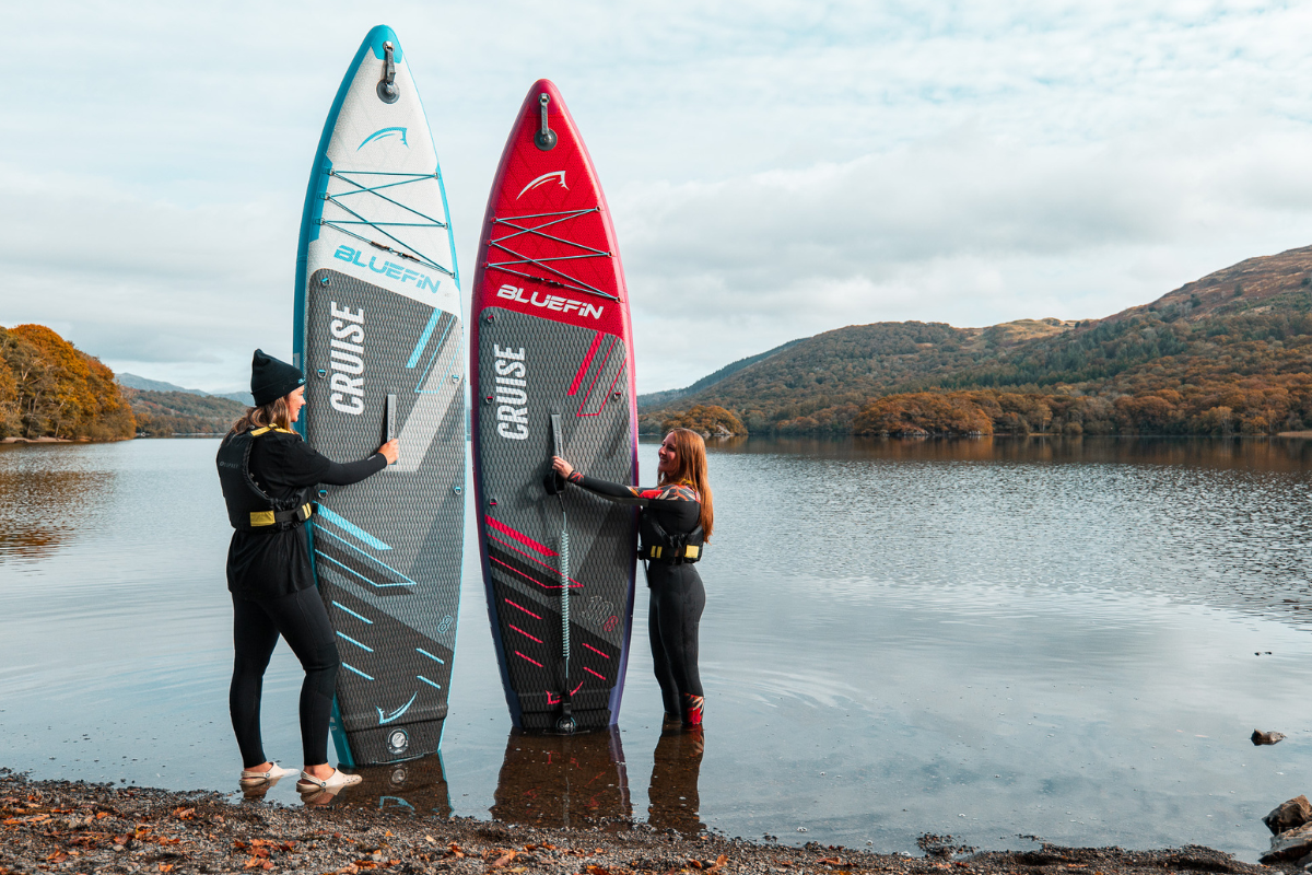 two people stood at the waters edge holding their paddleboards