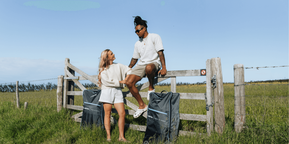 two people sat with their paddleboard bags on a fence 