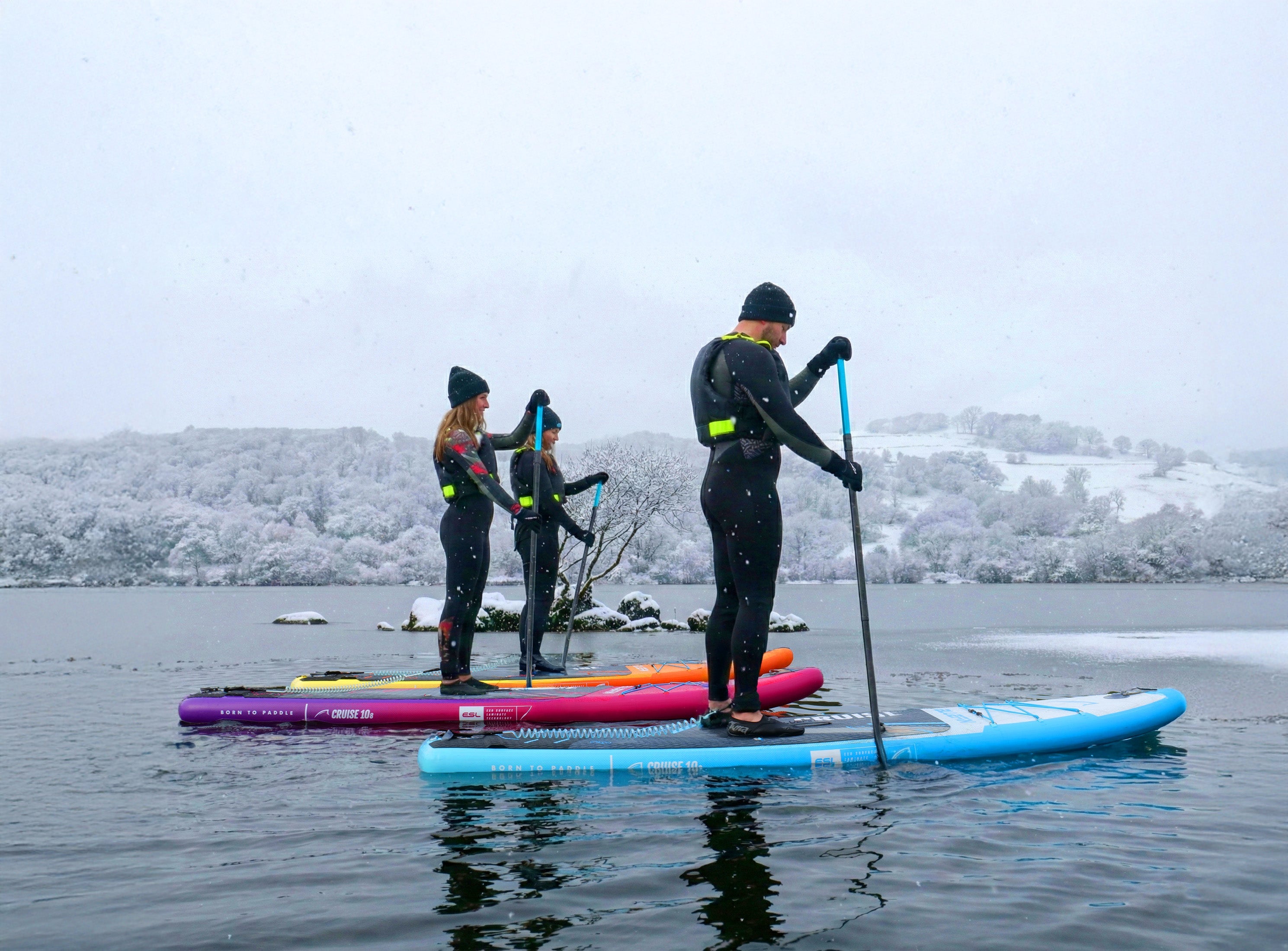three people paddleboarding in the snow 