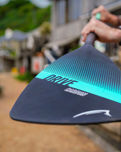 Close-up of a paddle with 'Drive Carbon' logo, held by a person outdoors.