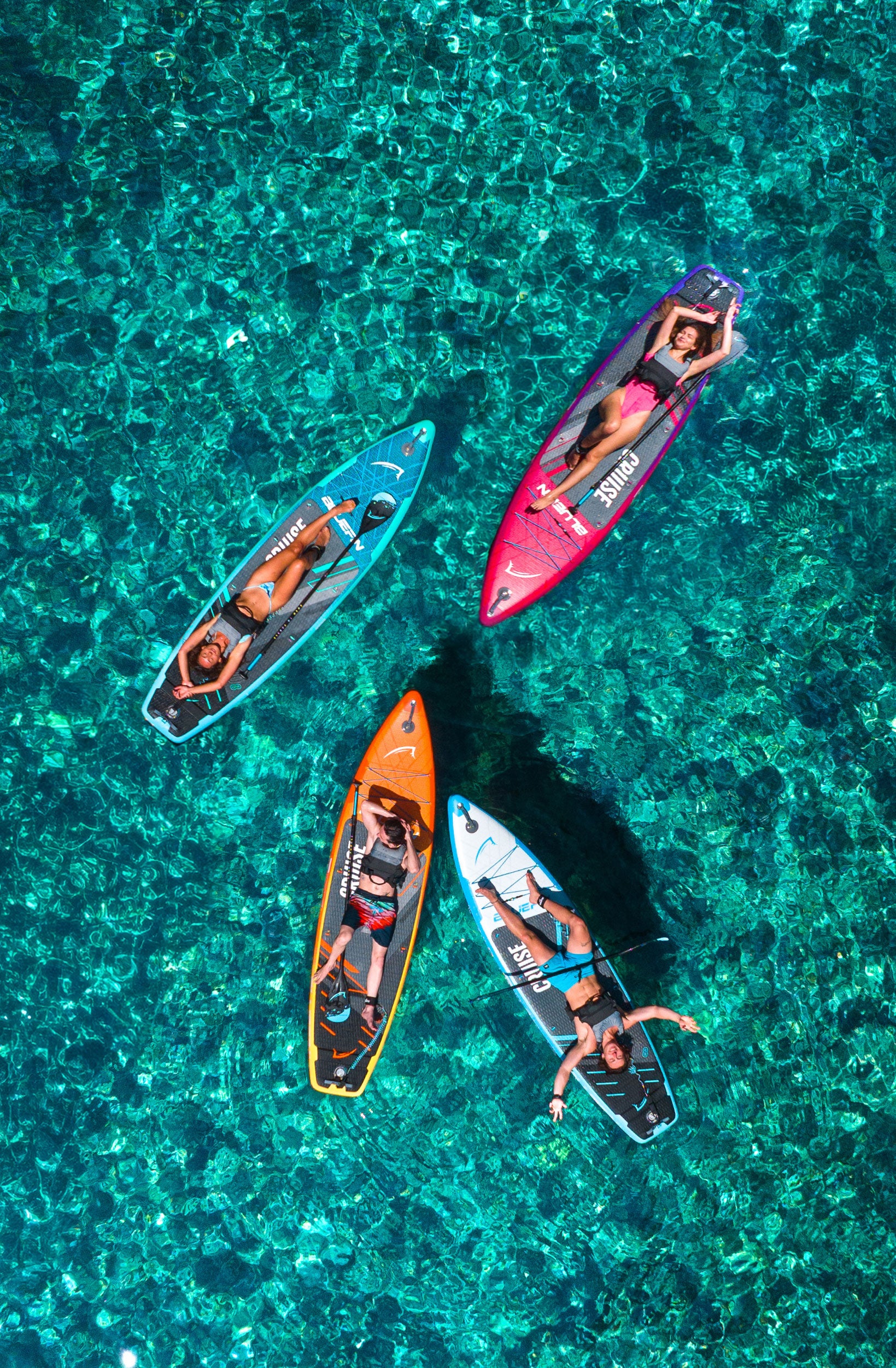 Four paddleboarders on colorful boards in clear water, enjoying a sunny day on the water.