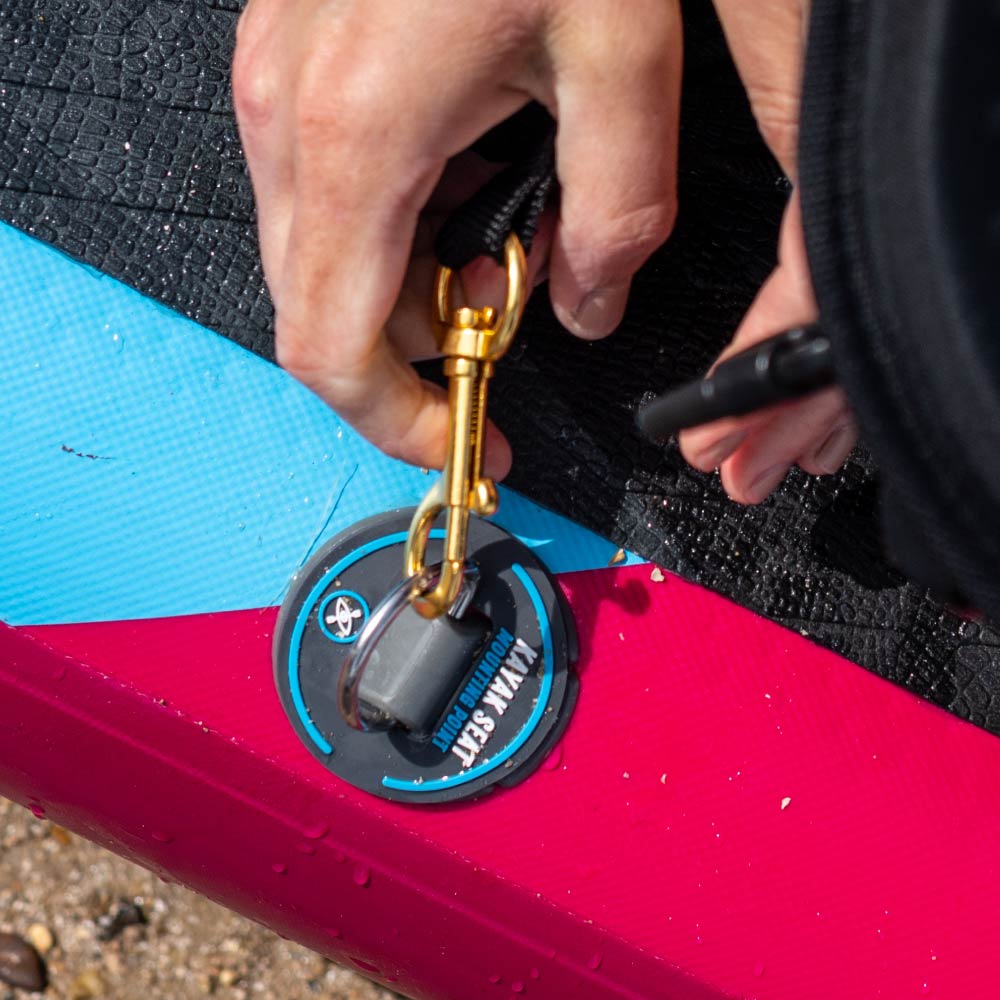 Hand securing a gold clip to a waterproof pad on a colorful paddleboard.