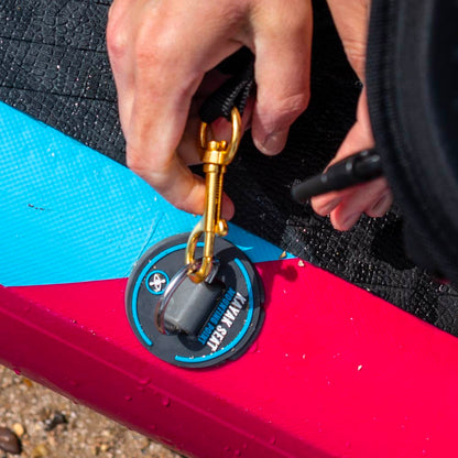 Hand securing a gold clip to a waterproof pad on a colorful paddleboard.