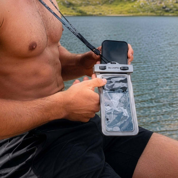 Waterproof phone pouch held by a man, with a phone inside, by a lake in nature.