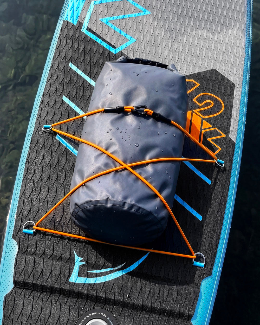Paddleboard with a dark waterproof bag secured by orange bungee cords on a textured surface