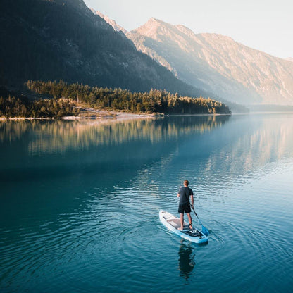 Person paddleboarding on calm lake with mountains and trees reflecting in the water