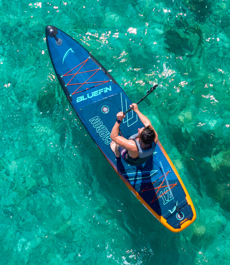 Paddleboard on clear water with a person paddling, featuring a textured deck and center fin.