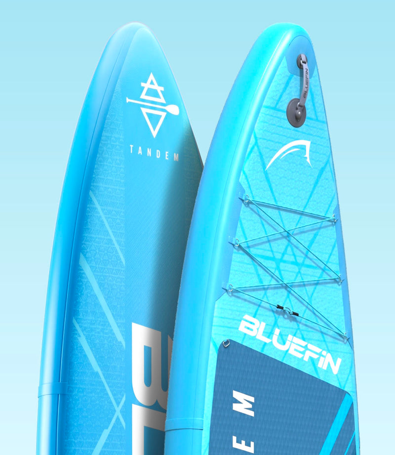 Two blue inflatable paddleboards with logos, one labeled TANDEM and the other BLUEFIN, angled for display.