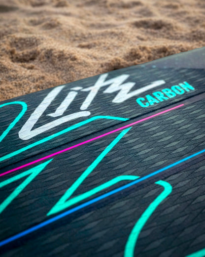 Close-up of a black paddleboard deck with colorful graphics and the word 'Carbon