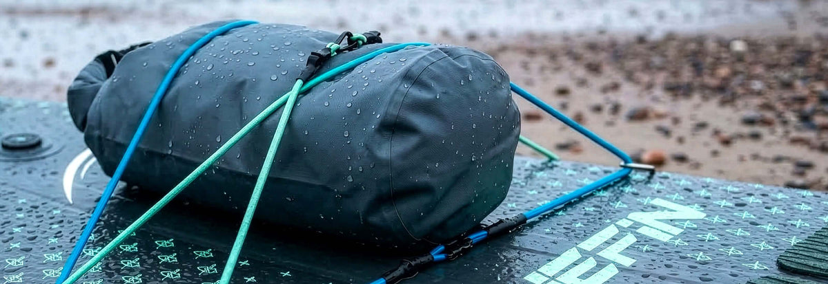 Dry bag secured on a paddleboard with blue straps, water droplets visible on the surface