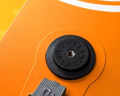 Close-up of an orange inflatable paddleboard's inflation valve and black fin attachment