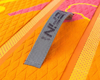 Textured orange paddleboard deck with gray handle strap and colorful design elements