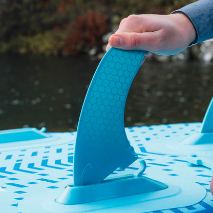 Hand inserting a blue fin into the base of an inflatable paddleboard on water.