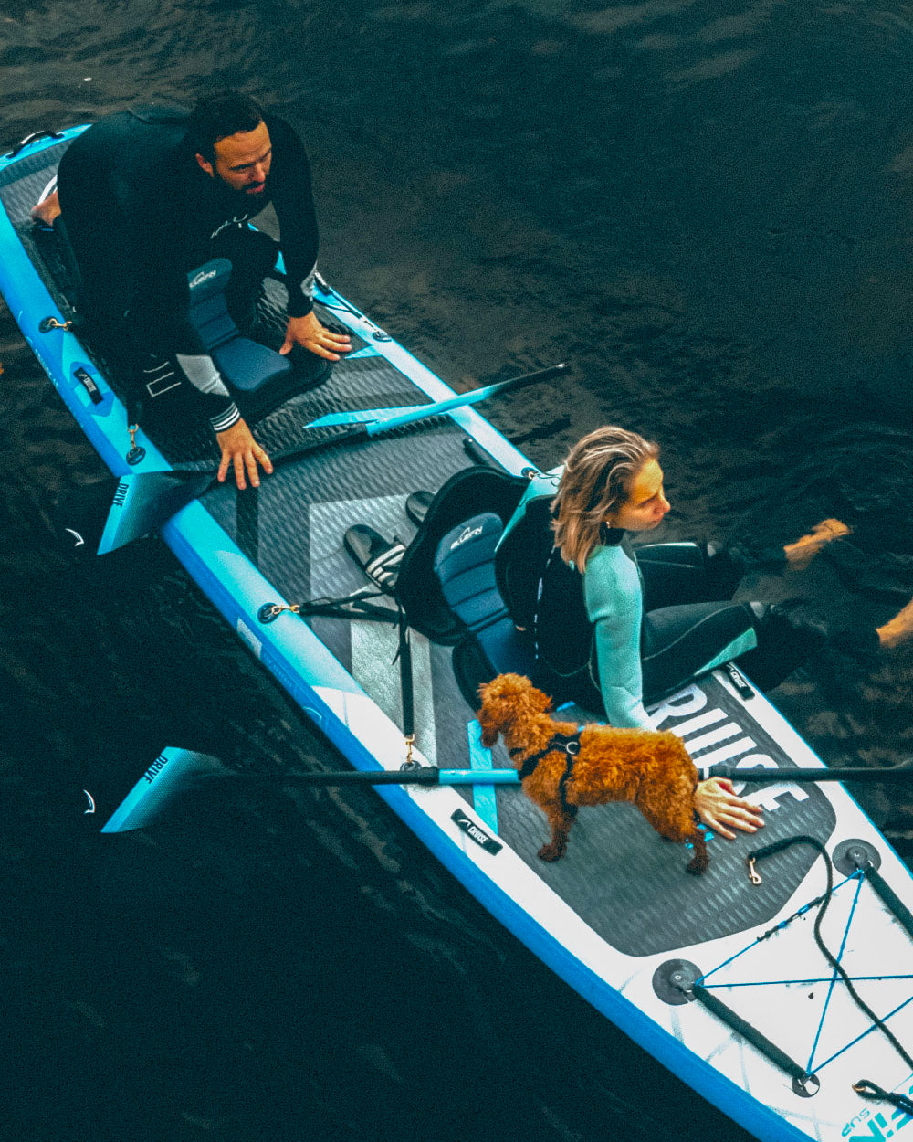Two people on a tandem stand up paddleboard with a dog